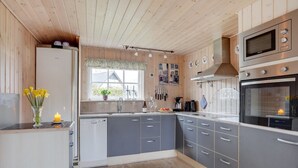 Une cuisine moderne avec des meubles gris, un four encastré et une fenêtre donnant sur l’extérieur.
