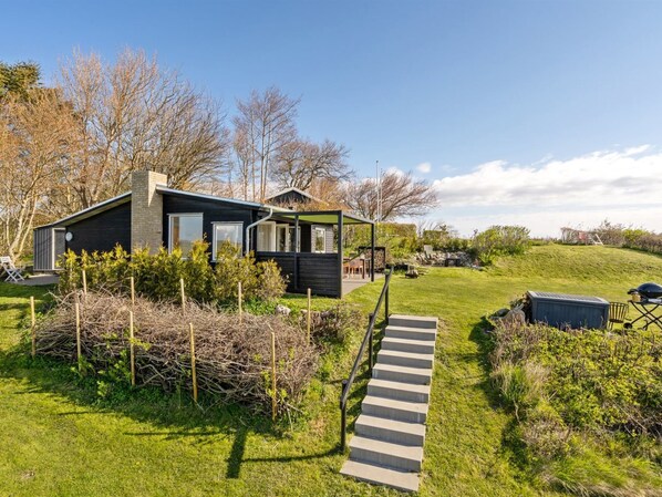 Una casa moderna con un espacio exterior cubierto, un jardín césped y una escalera que conduce a la entrada.