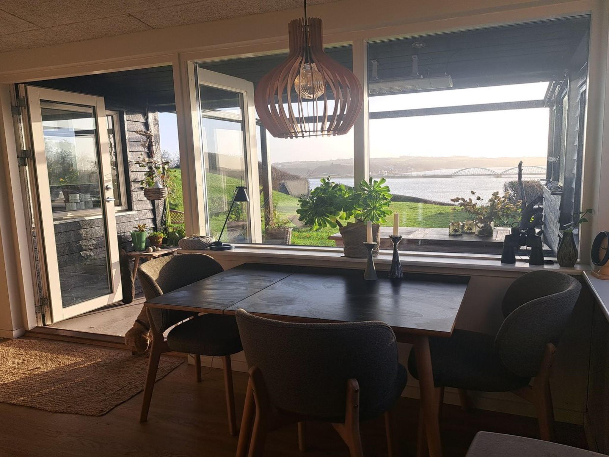 Un espace repas comprenant une table, des chaises et une vue sur un pont et le paysage, grâce à de grandes fenêtres.