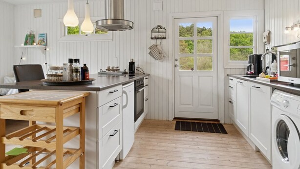 A modern kitchen with white cabinetry, a built-in oven, a microwave, and a sink. There is a wooden table with a wine rack and a hanging light fixture above it. - "Aris" - 480m from the sea by Interhome (Ebeltoft)