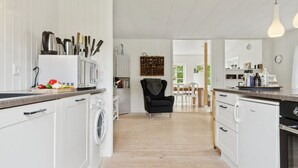A modern kitchen with white cabinetry, a washing machine, and a dining area with a black chair and white table. - "Aris" - 480m from the sea by Interhome (Ebeltoft)