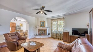 Un salon spacieux avec des canapés en cuir, une table basse en bois, un ventilateur de plafond, une cheminée et un téléviseur.