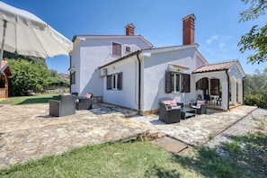 Uma casa com um alpendre, móveis de exterior e um guarda-sol branco.