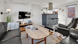 Un salon moderne doté d’un téléviseur à écran plat, de canapés en cuir, d’une table basse en bois et d’un coin cuisine avec un tabouret de bar.