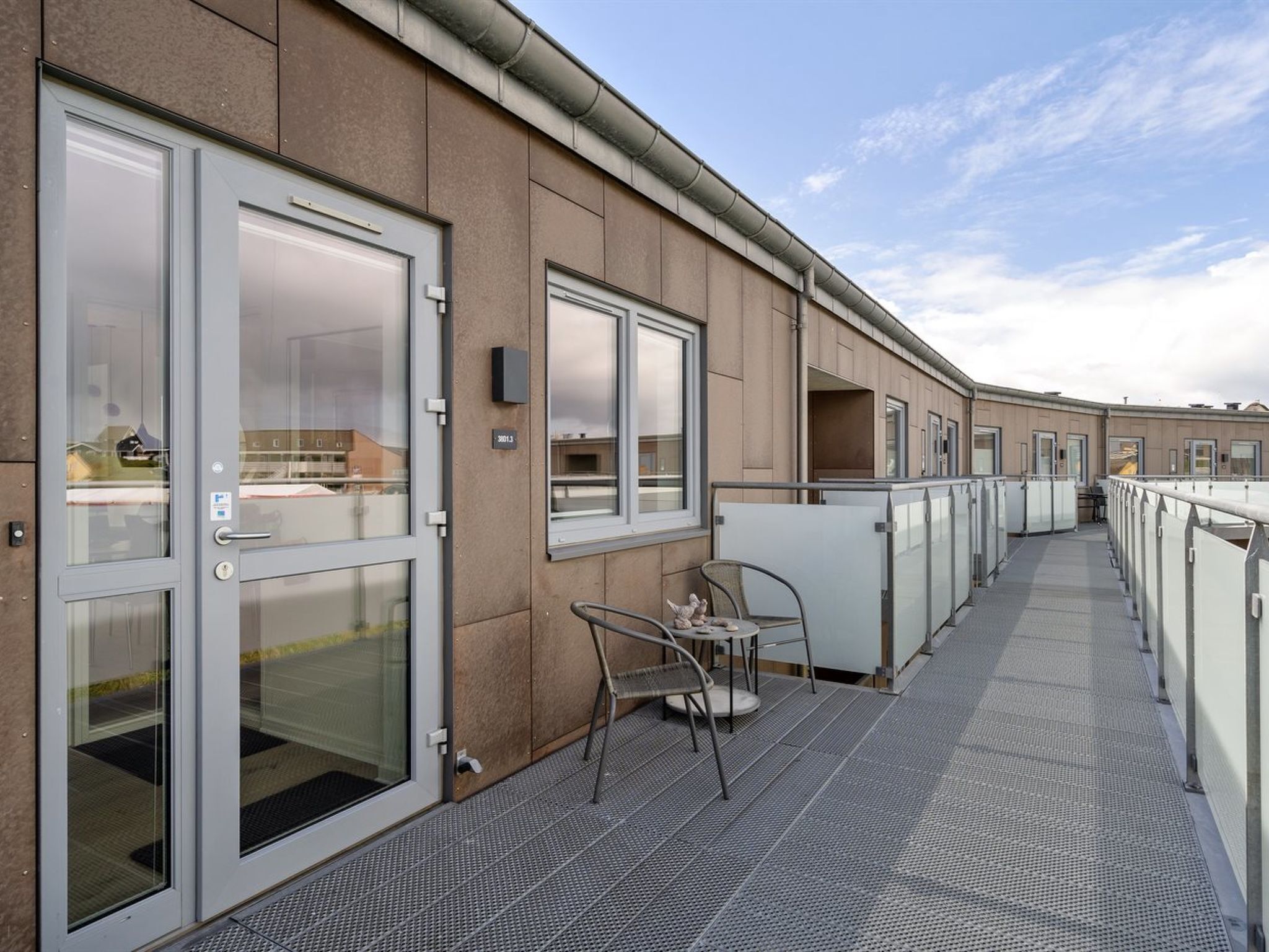 A corridor with glass doors, a metal railing, and a seating area with chairs and a table.