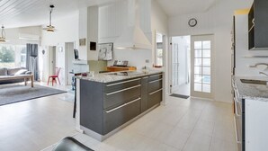 Una cocina moderna con una isla central, muebles blancos y un amplio ventanal que proporciona luz natural.