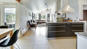 Una cocina moderna con una isla central, una zona de comedor con mesa y sillas, y una sala de estar con sofá y mesa de centro.