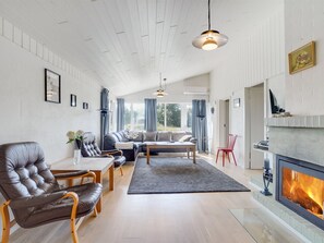 Ett rymligt vardagsrum med en öppen spis, läderfåtöljer, en soffa och en matplats.