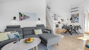 Una sala moderna con un sofá seccional gris, una mesa de centro redonda con un frutero, y una escalera que lleva a una cocina.