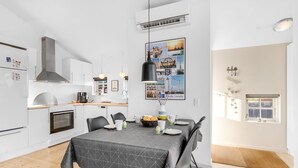 Una cocina moderna con armarios blancos, horno empotrado y comedor con mesa para cuatro.