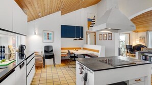 Una cocina moderna con una isla central, un comedor con un banco y una escalera que sube a un nivel superior.