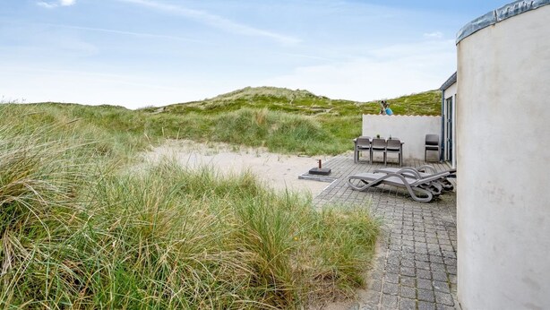 Un edificio frente a la playa con un patio, asientos exteriores y vistas a las dunas.