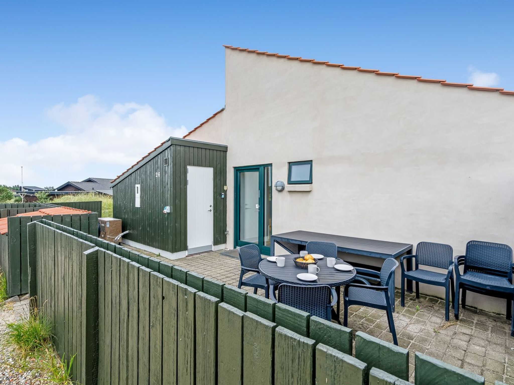 Un espace patio avec une table et des chaises, un petit abri de jardin et une clôture en bois.