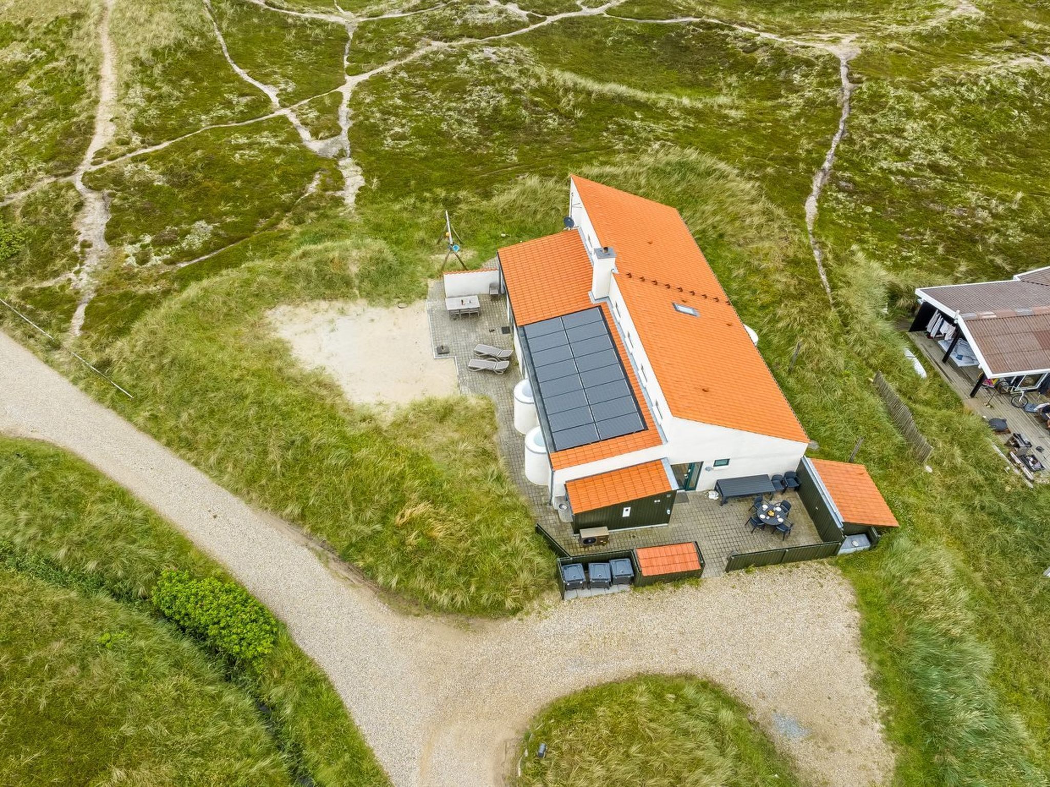 Vue aérienne d’une maison moderne avec un toit rouge, des panneaux solaires et une allée gravillonnée.