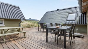 En træterrasse med et bord, stole og et picnicbord, samt et vindue.