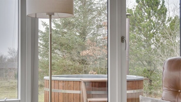 A room with a large window, a wooden hot tub, and a leather chair.
