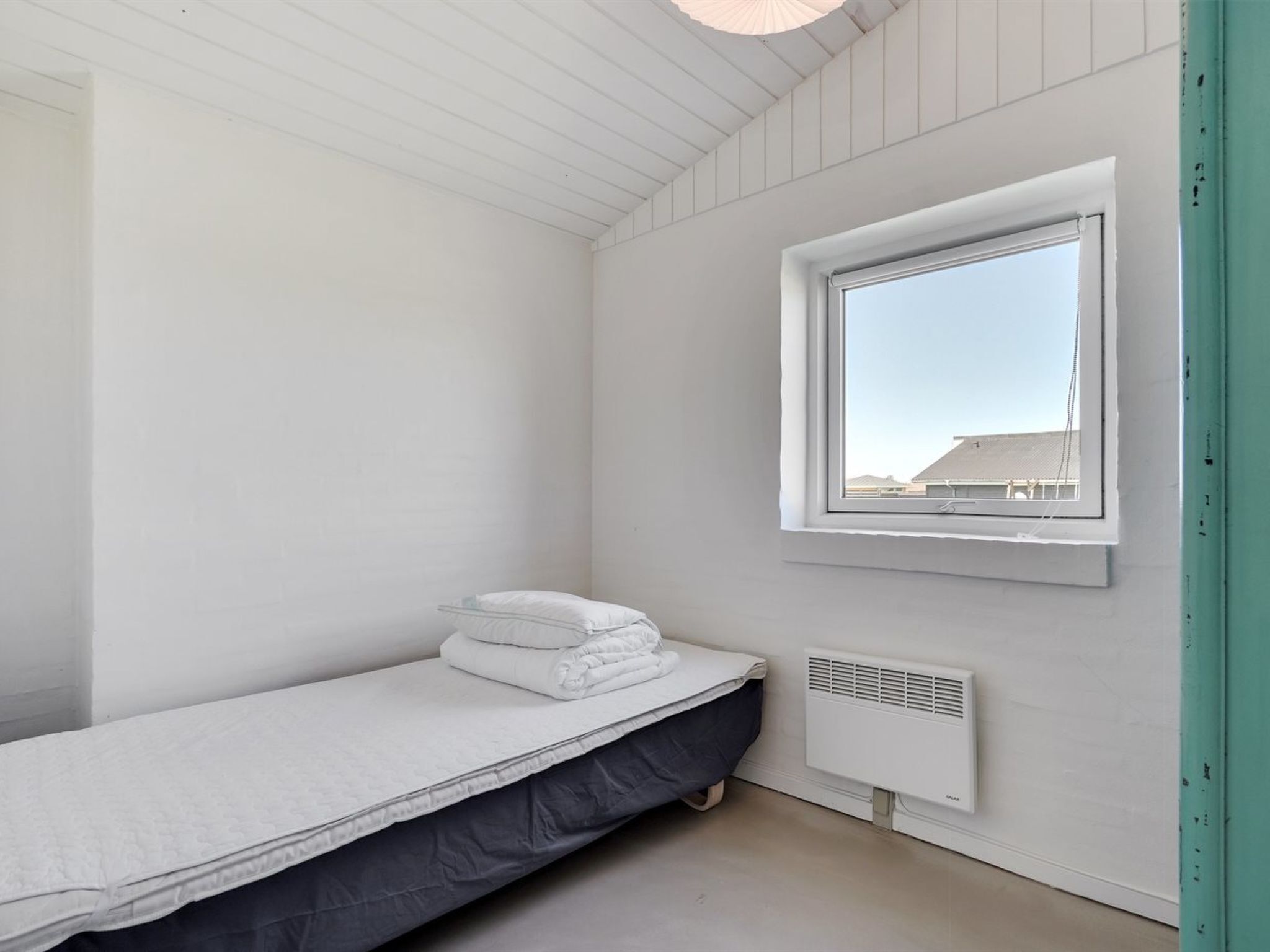 A small, clean room with a single bed, a window, and a white radiator.