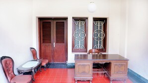 Una habitación con un escritorio de madera, dos sillas, una mesita y dos puertas con celosías metálicas decorativas.