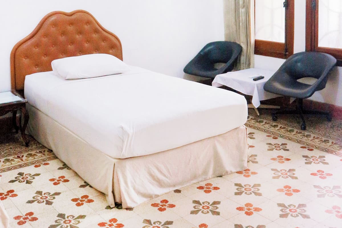 Quarto de hotel com cama, duas cadeiras, uma janela e piso estampado.
