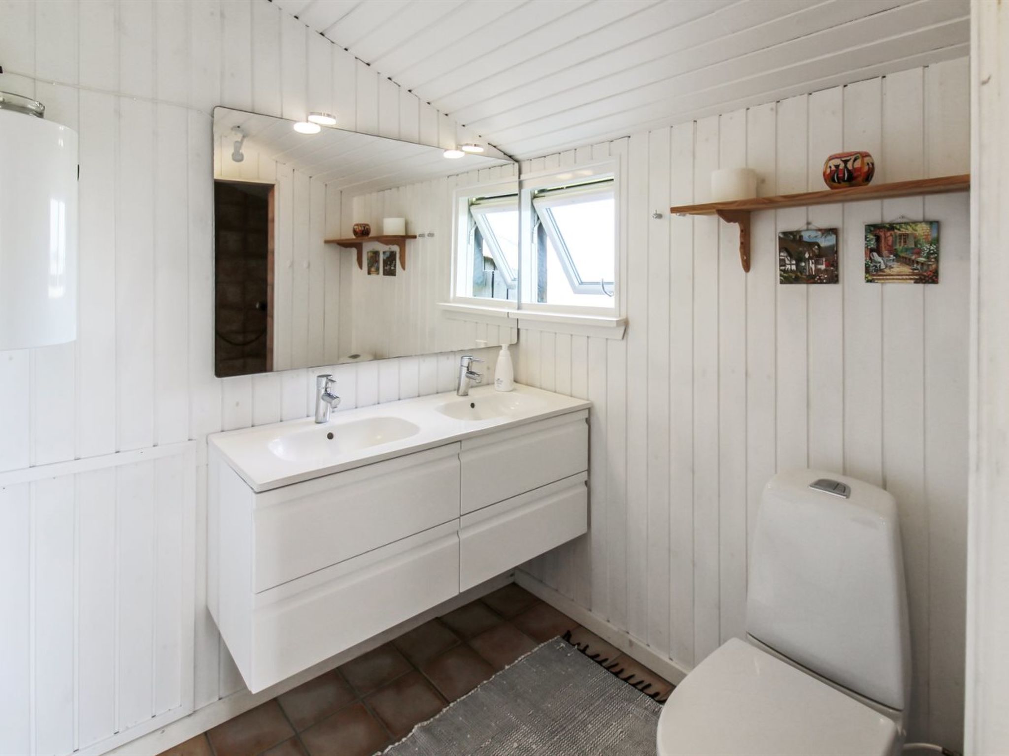 Ein Badezimmer mit weißem Holzvertäfelung, einem Doppelwaschtisch, einer Toilette und einem Fenster mit Blick.