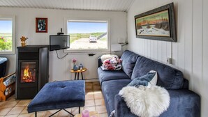 Un salon confortable avec une cheminée, un canapé, un téléviseur et une fenêtre donnant sur une route où l’on aperçoit une voiture.