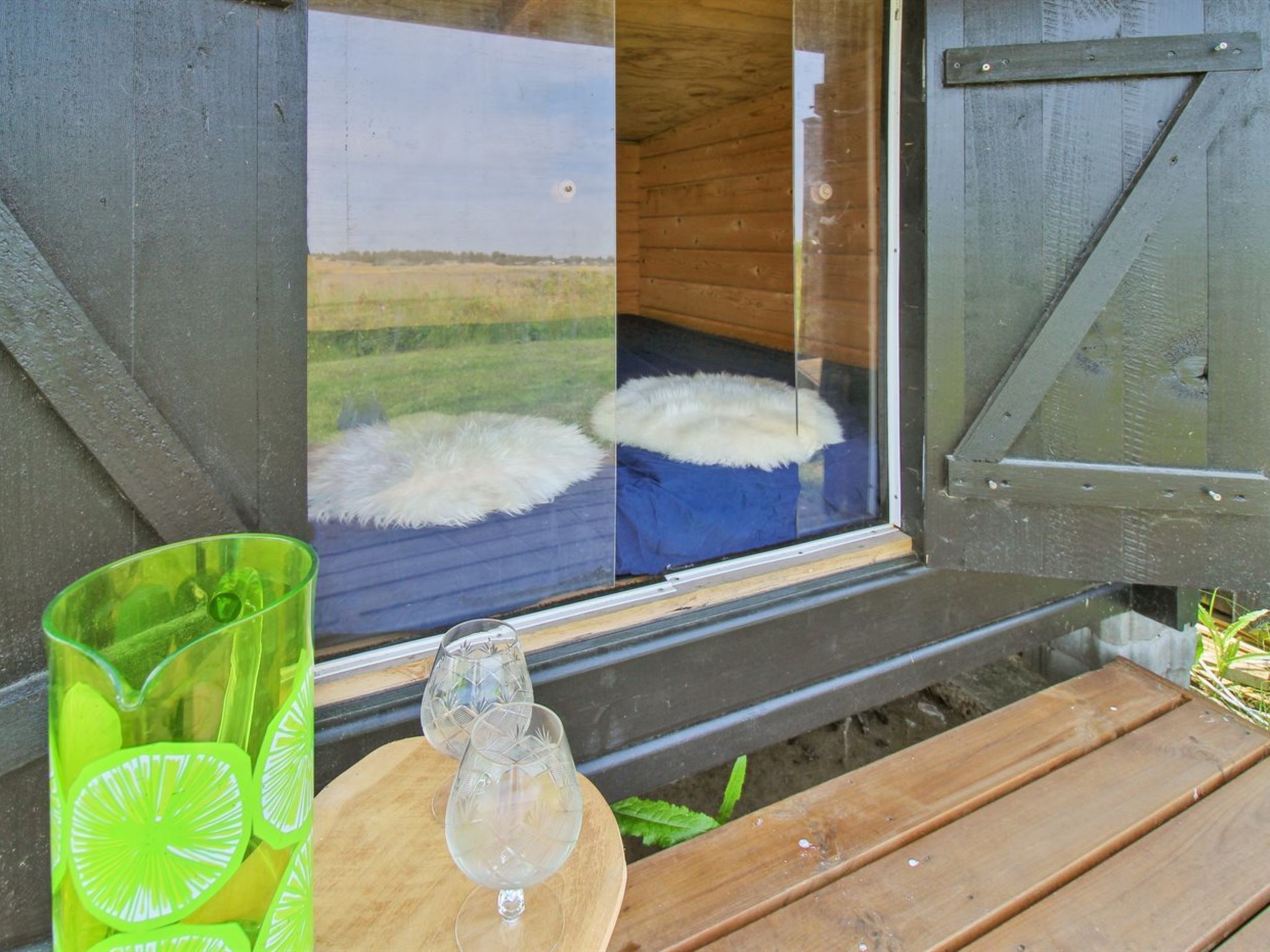 Une cabane en bois avec une grande fenêtre, une table en bois et un pichet en verre vert contenant des rondelles de citron vert.
