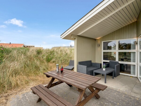 Un patio al aire libre con mesa y asientos de madera, con vistas a un campo cubierto de césped.