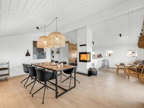 A spacious dining area with a wooden table and black chairs, a kitchen with a large TV, and a living area with a sofa and wicker furniture.