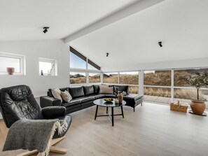 Ein modernes Wohnzimmer mit einem Ecksofa, einem runden Couchtisch und großen Fenstern mit Blick ins Freie.