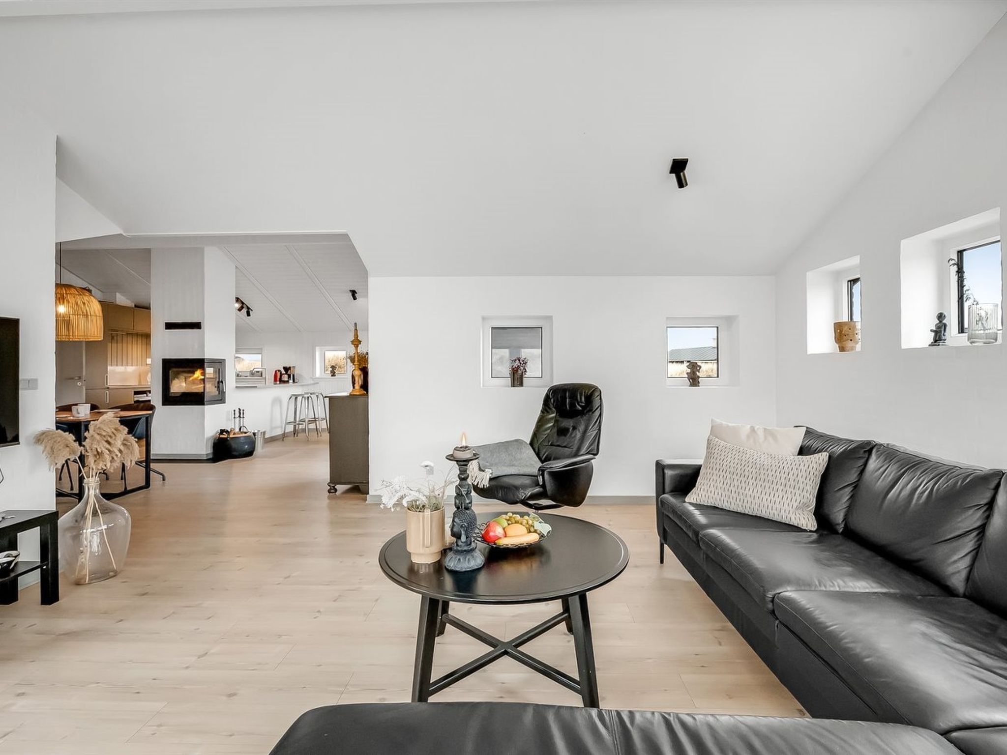 A modern living room with a leather sofa, a coffee table with fruits, and a dining area in the background.
