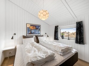 Une chambre à coucher avec un lit, un tableau, une fenêtre avec des rideaux et un luminaire suspendu.