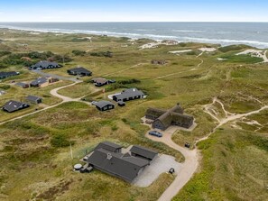 Une vue aérienne d’une propriété côtière comprenant plusieurs bâtiments, dont une structure remarquable avec un toit de chaume, le tout entouré d’un terrain herbeux et offrant une vue dégagée sur l’océan.