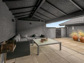 An outdoor patio area with a sofa, a table, and potted plants.