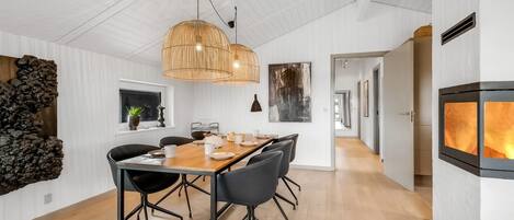 A modern dining area with a wooden table and chairs, a hanging light fixture, and a stone wall feature.