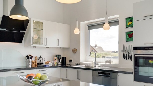 Une cuisine moderne avec des meubles blancs, un grand îlot central agrémenté d’un panier de fruits, une machine à café et un four Siemens.
