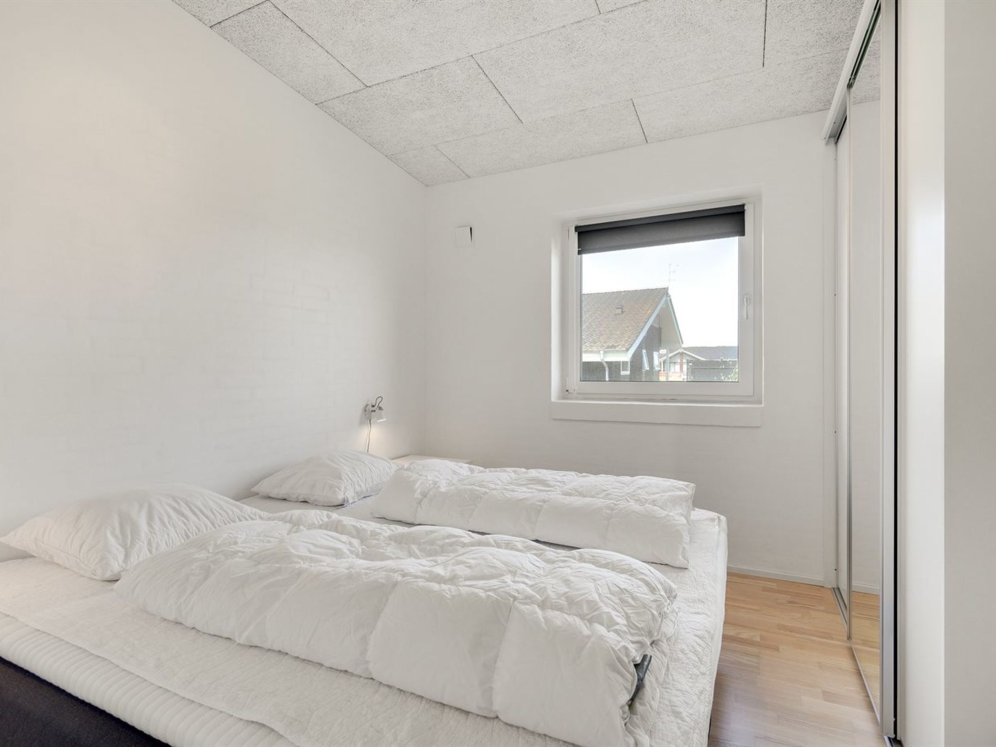 Camera da letto minimalista con un grande letto, una finestra e vista su una casa.