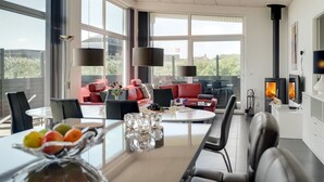 Un salon moderne doté d’une cheminée, de grandes fenêtres et d’un coin repas agrémenté de fruits et de verres.