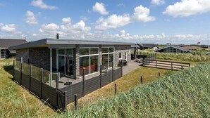 Une maison moderne dotée d’une façade en verre, d’une terrasse et offrant une vue sur le paysage environnant.