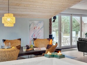 Een eethoek met rieten stoelen, een houten tafel, een hanglamp en uitzicht op de omgeving door grote ramen.