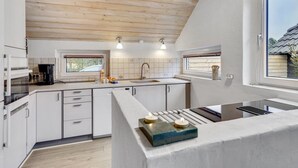 Une cuisine moderne avec des poutres en bois au plafond, des meubles blancs et un grand îlot central doté d’un évier intégré.