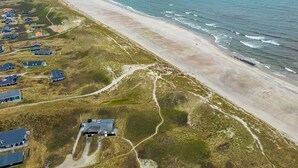 An aerial view of a coastal area with a sandy beach, a few houses, and a clear view of the ocean.