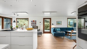 A modern kitchen with white cabinetry, a central island, and a dining area with a blue sofa and wooden table.