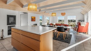 Cocina moderna con una isla central, armarios de madera y una zona de comedor con una silla roja y una mesa.