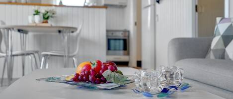 A modern kitchen with white cabinets, a dining area with a white table and chairs, and a living area with a grey sofa.