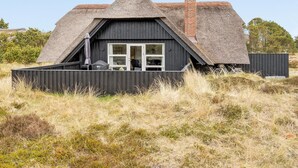 A thatched-roof house with a black exterior, a chimney, and a small deck with outdoor furniture. - "Vladan" - 1.6km from the sea by Interhome (Blåvand)