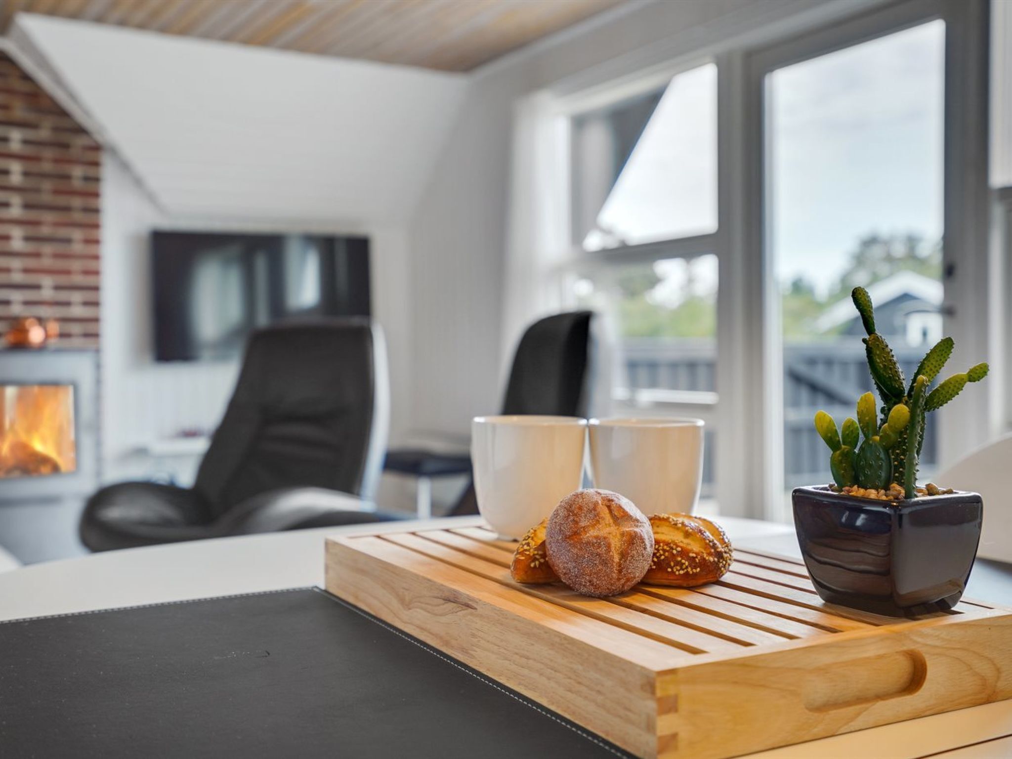 Un salon moderne avec une table basse en bois, deux tasses, un cactus en pot et une miche de pain.