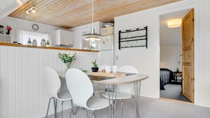A modern kitchen with white cabinetry, a wooden ceiling, and a dining area with white chairs and a round table. - "Vladan" - 1.6km from the sea by Interhome (Blåvand)