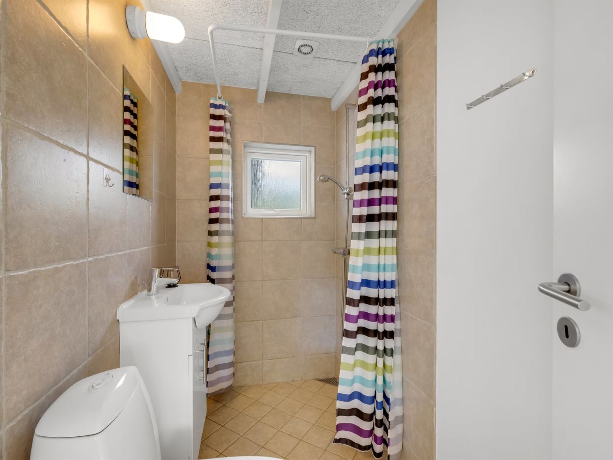 A bathroom with a toilet, a sink, a shower curtain, and a window.