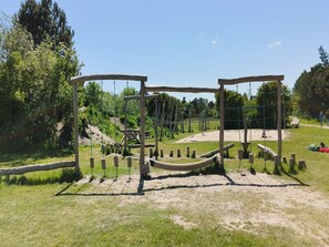 Un terrain de jeux doté de structures en bois et de cordes, entouré d’herbe et d’arbres.