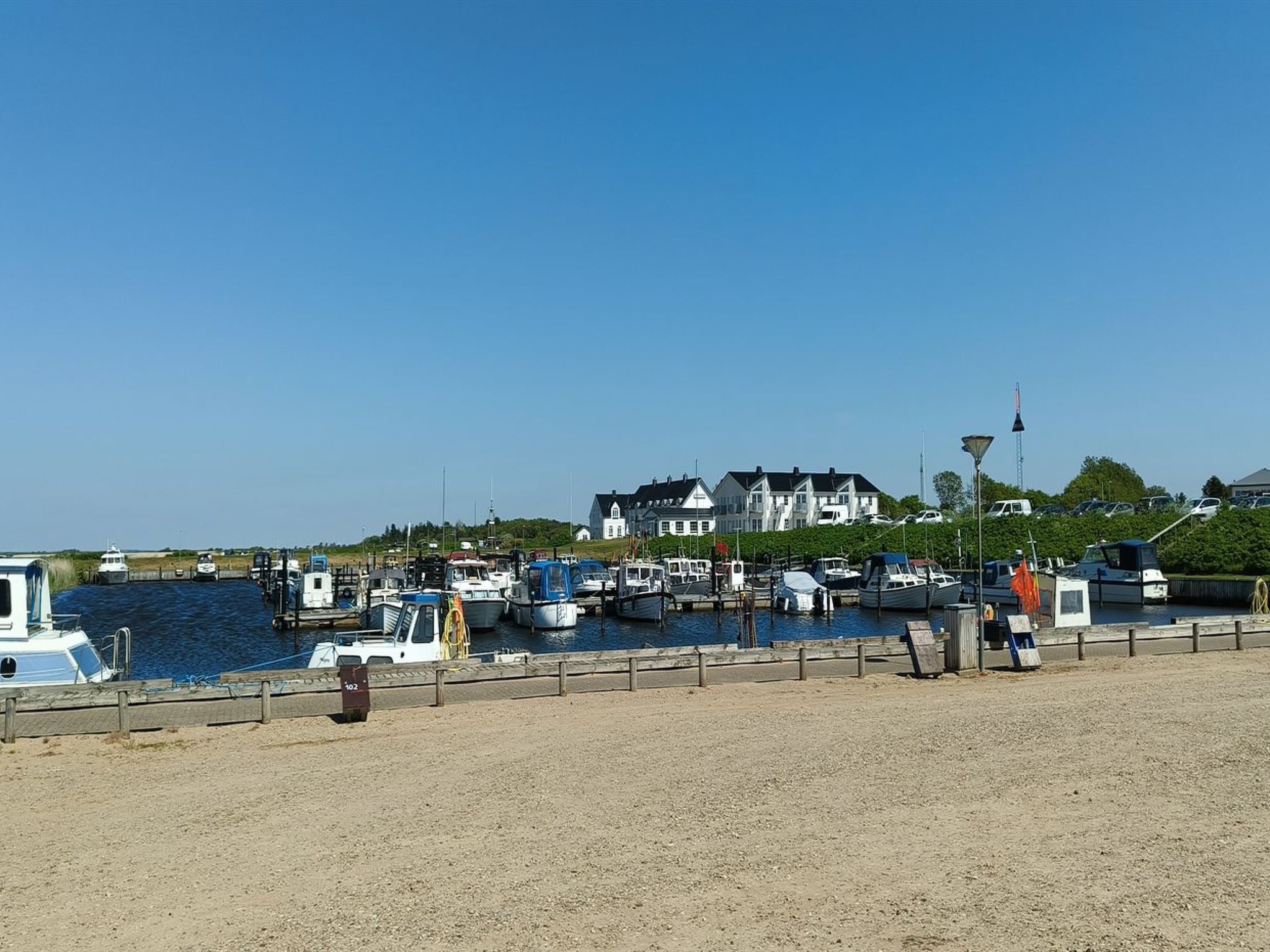 En småbåtshamn med förtöjda båtar, en sandstrand och hus i bakgrunden.